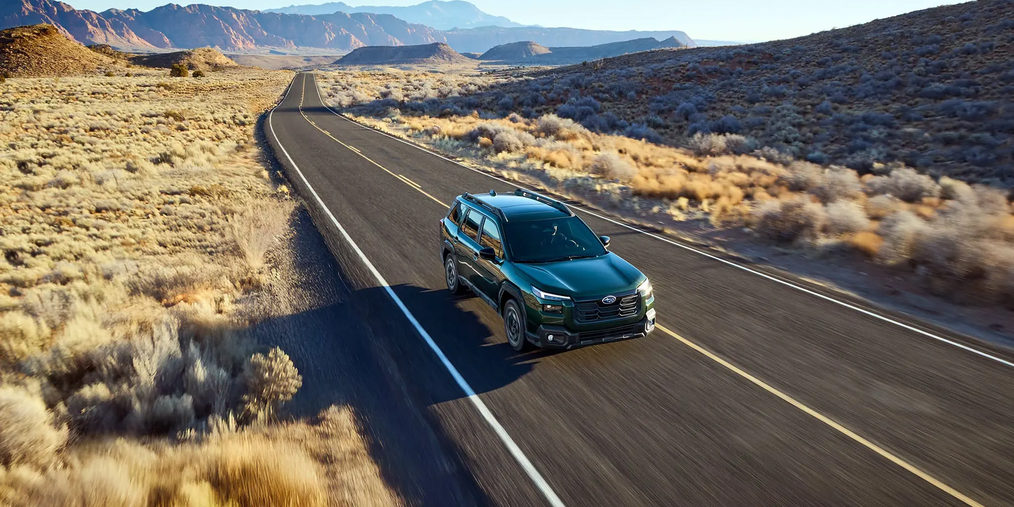 A Subaru Forester driving down an empty two-lane highway that runs straight to the horizon through open country.
