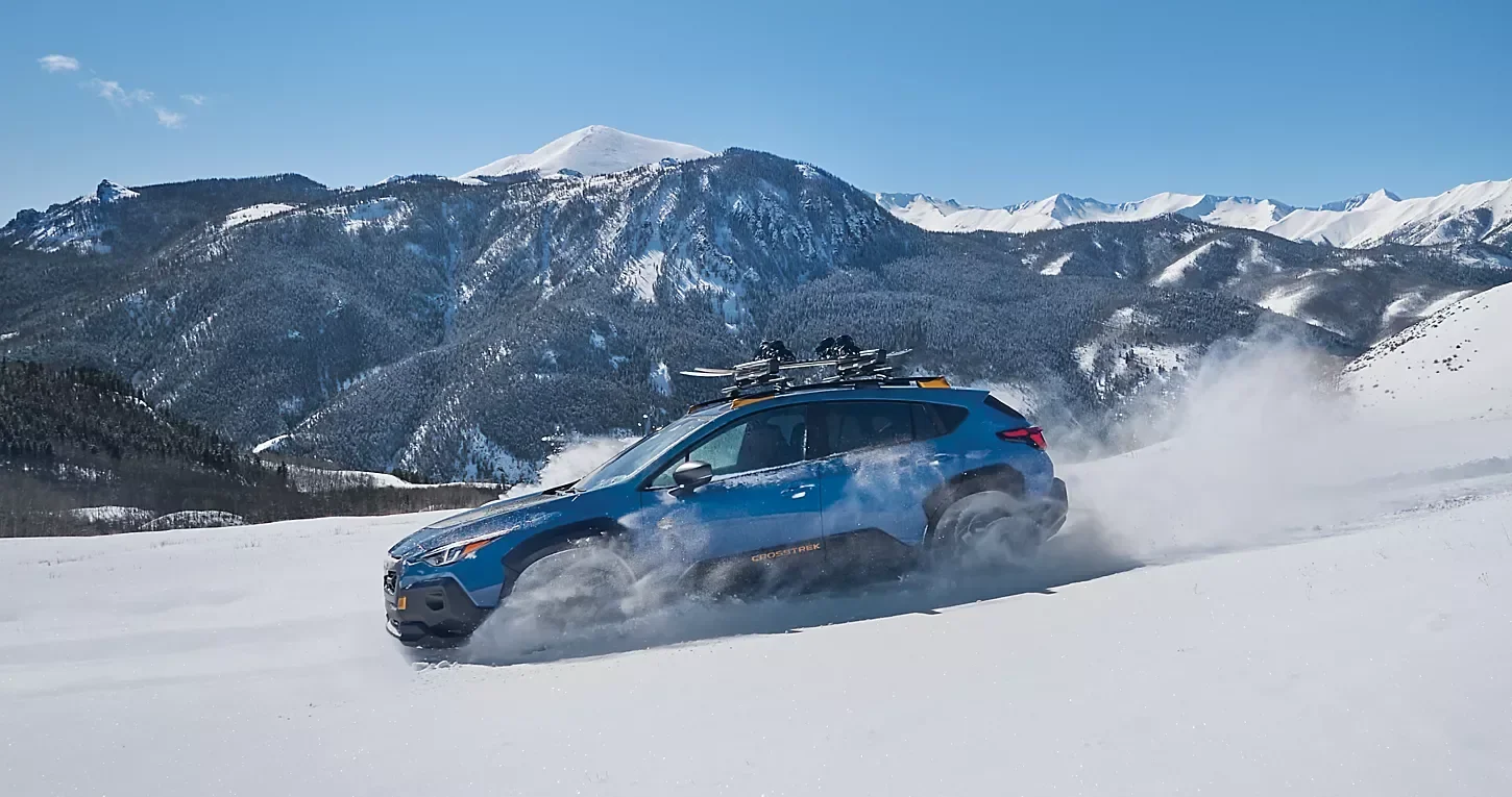 A blue Subaru driving over snow, with mountains behind it.