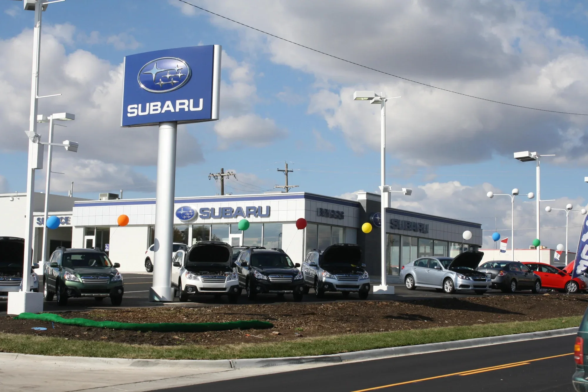 A Subaru dealership building with a tall Subaru sign, vehicles parked across the lot in front of it.