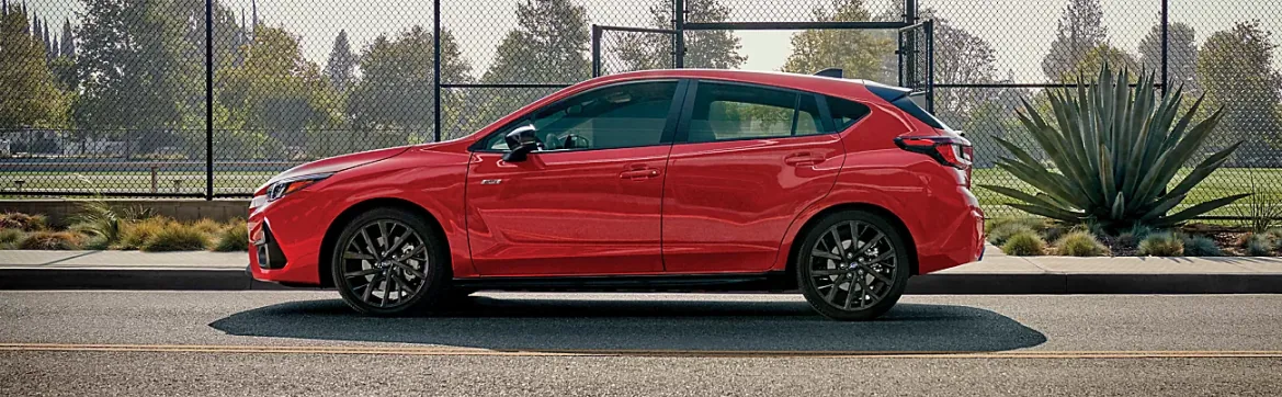 Red Subaru in profile alongside a park fence