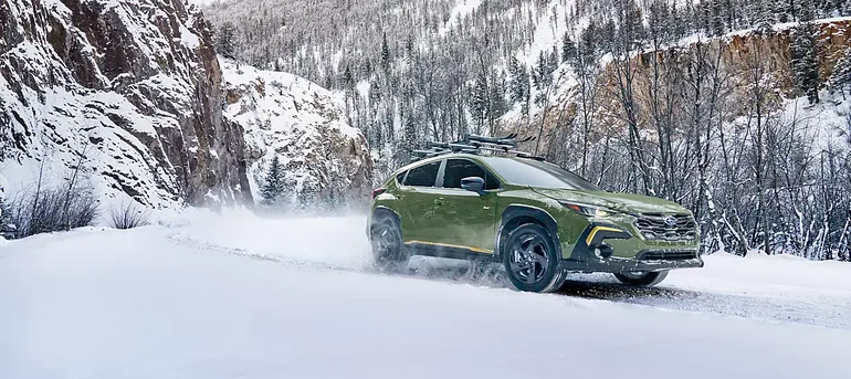 Green 2026 Subaru Crosstrek driving through deep snow on a mountain pass