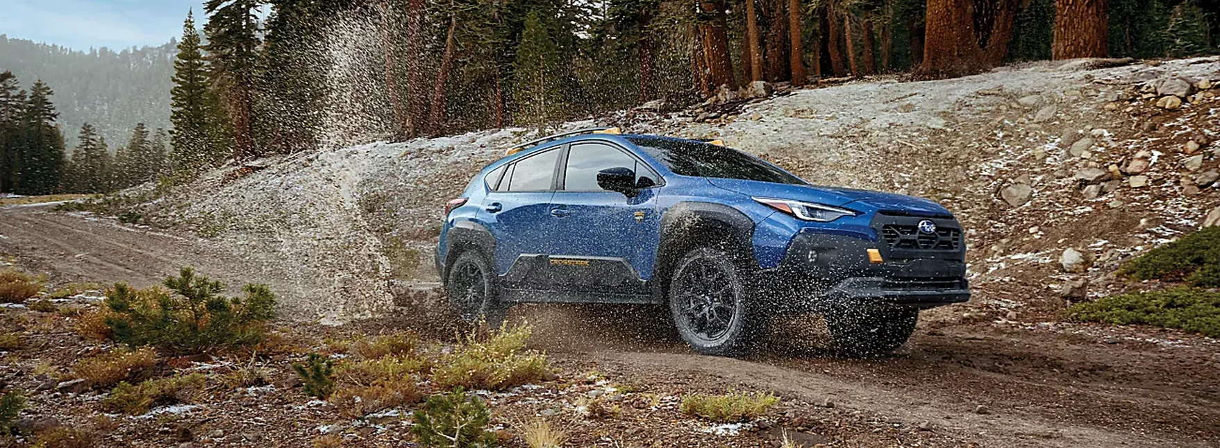 Blue 2026 Subaru Crosstrek Wilderness splashing through a rocky forest trail