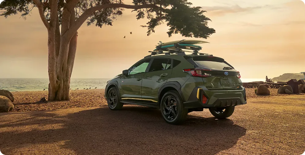 Green 2026 Subaru Crosstrek with roof rails and a loaded roof basket at a beach campsite
