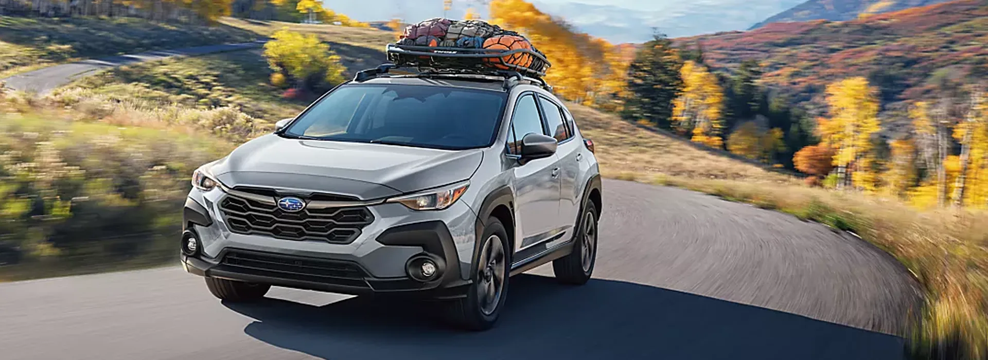 Silver 2026 Subaru Crosstrek with a loaded roof basket on a mountain road