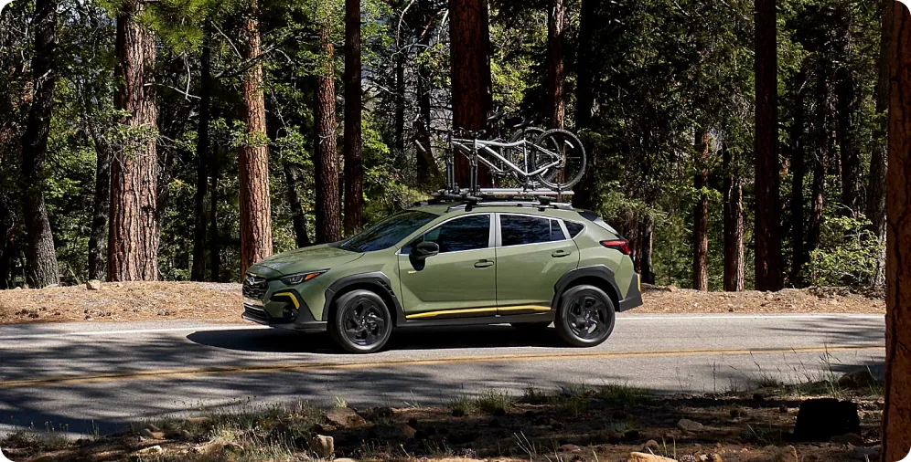 Green 2026 Subaru Crosstrek with a bike on the roof on a quiet forest road