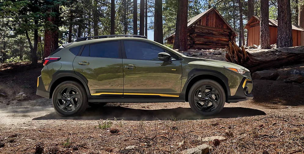 Green 2026 Subaru Crosstrek parked beside a log cabin in the woods