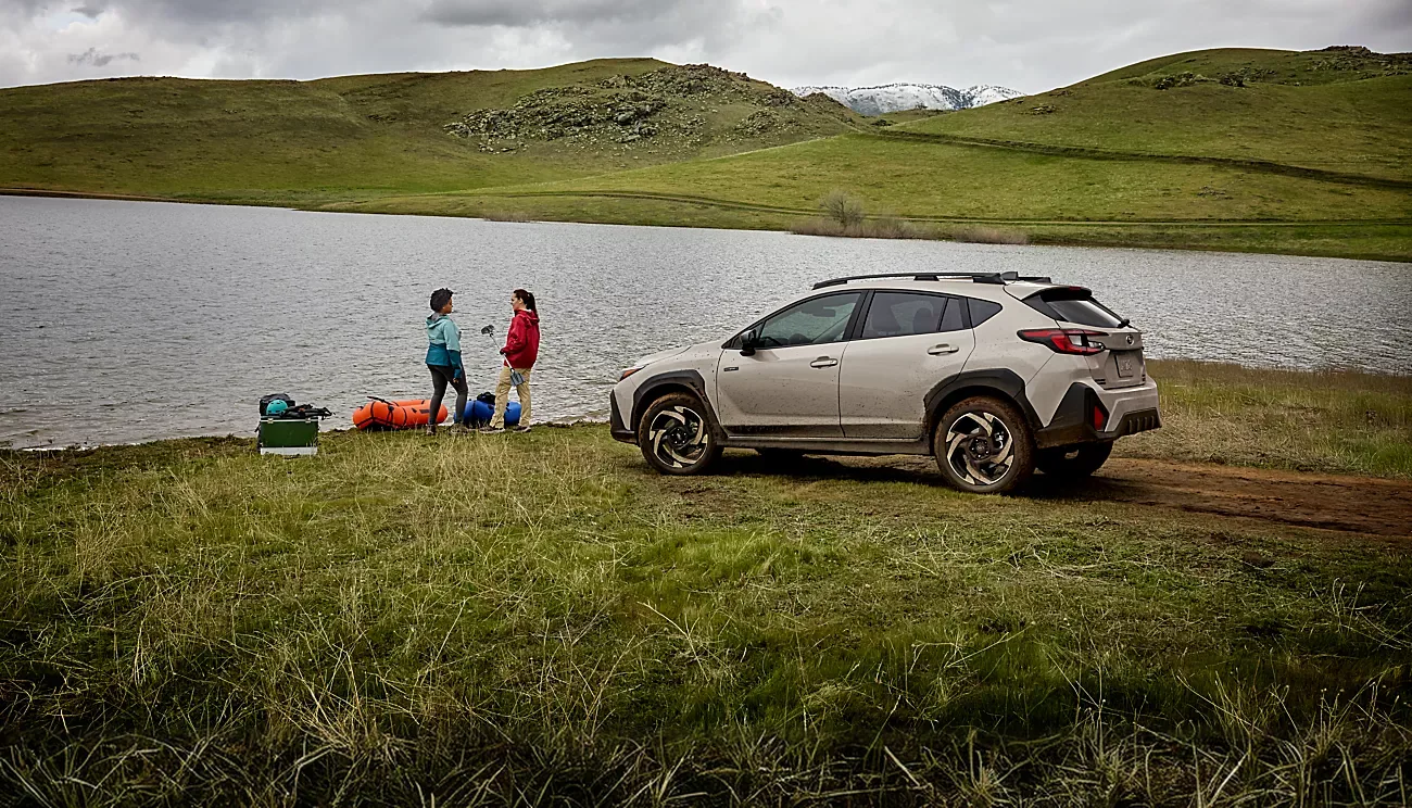 2026 Subaru Crosstrek Hybrid parked beside a lake while two people unload gear