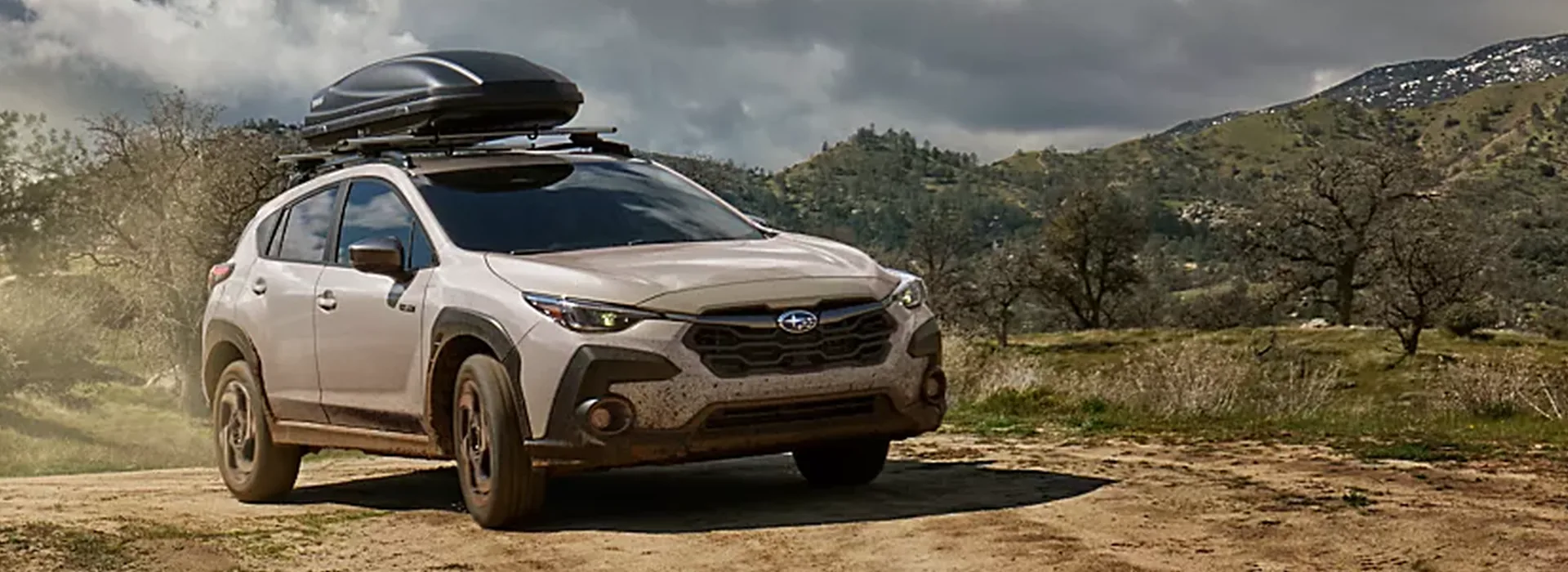 Sand-coloured 2026 Subaru Crosstrek Hybrid with a rooftop cargo box on a dirt trail
