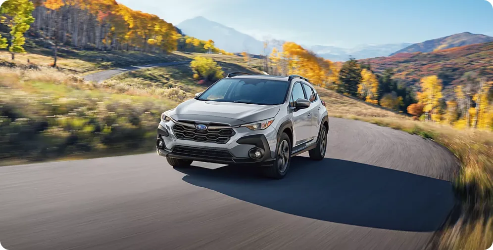 Silver 2026 Subaru Crosstrek Hybrid on a winding road above an autumn valley