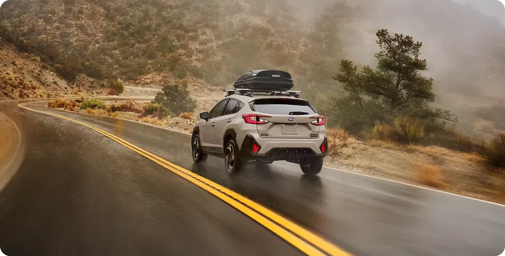 2026 Subaru Crosstrek Hybrid with a rooftop cargo box on a wet mountain highway