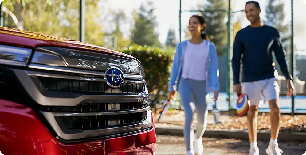 Couple walking past the front grille of a red 2026 Subaru Forester
