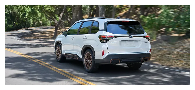 White 2026 Subaru Forester driving on a tree-lined road