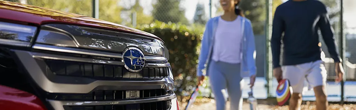 Couple walking past the grille of a red 2026 Subaru Forester