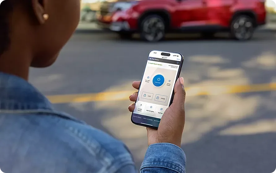 Owner using the MySubaru app on a smartphone beside a 2026 Subaru Forester Hybrid