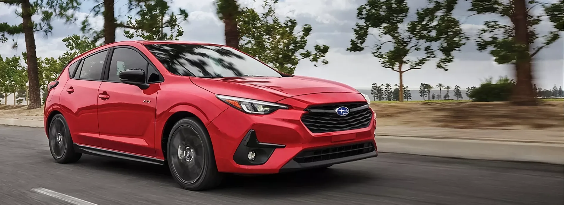 Red 2026 Subaru Impreza hatchback on a tree-lined road