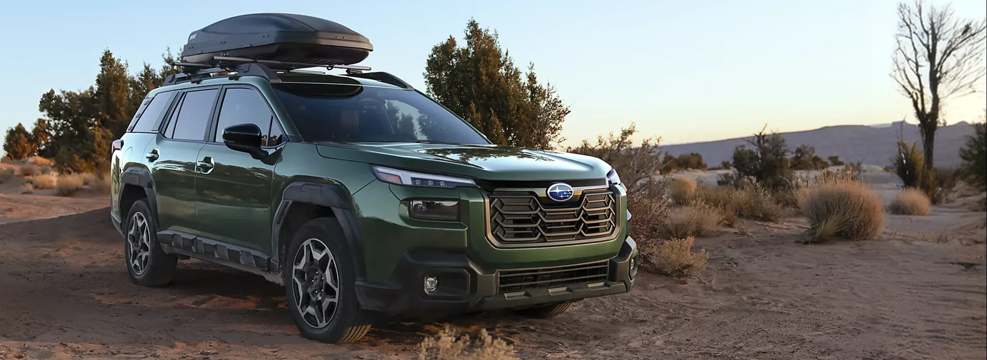 2026 Subaru Outback with a roof cargo box parked on a desert trail at sunset