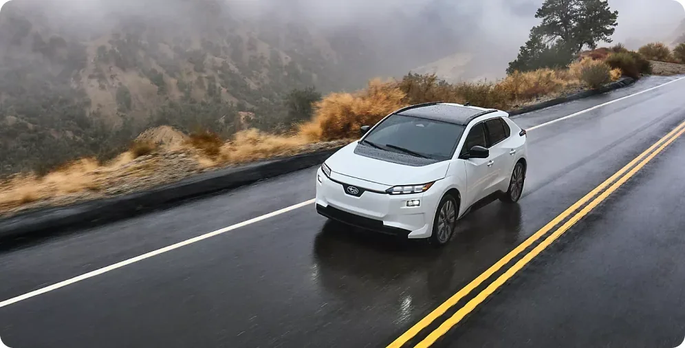 White 2026 Subaru Solterra driving a rain-soaked highway
