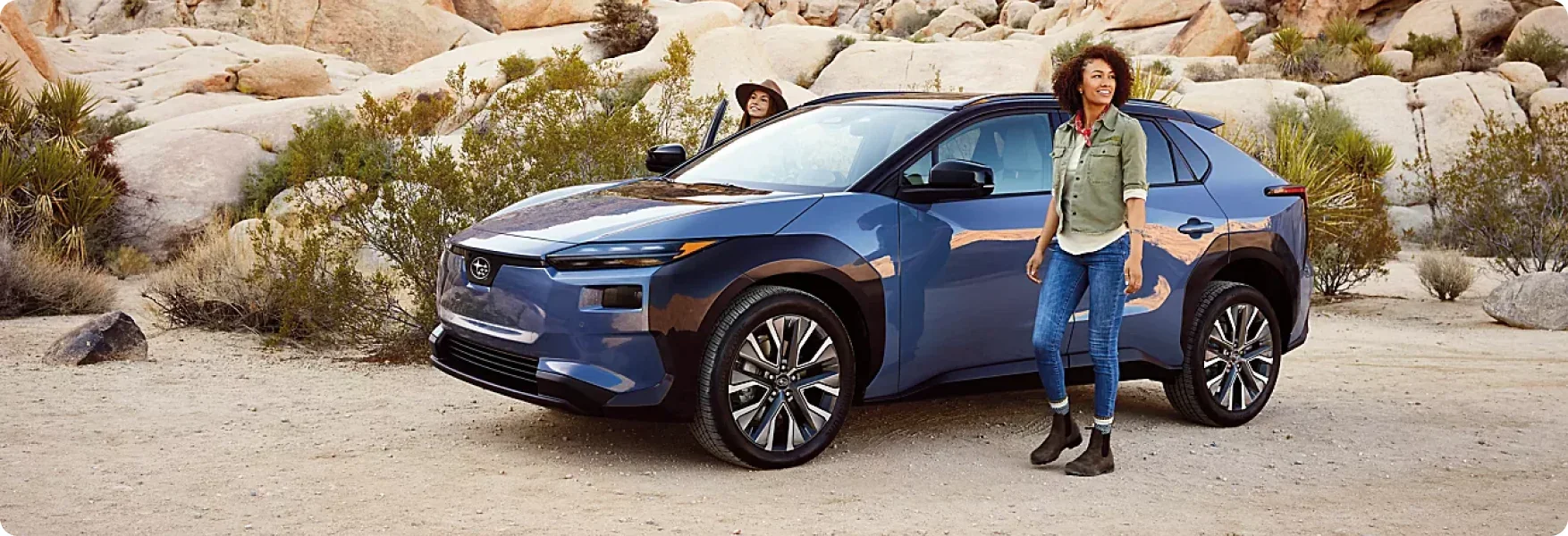 Two travellers beside a blue 2026 Subaru Solterra in the desert