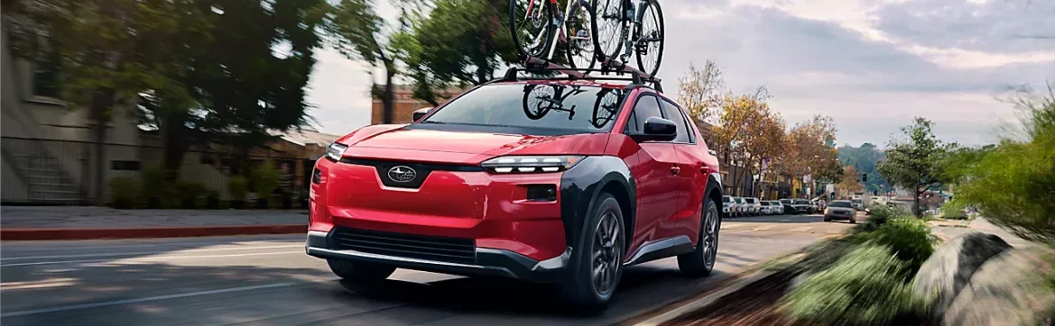 Red 2026 Subaru Solterra carrying bicycles through a town centre