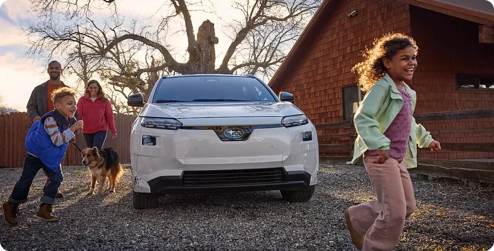 Family walking to a white 2026 Subaru Solterra parked outside a home