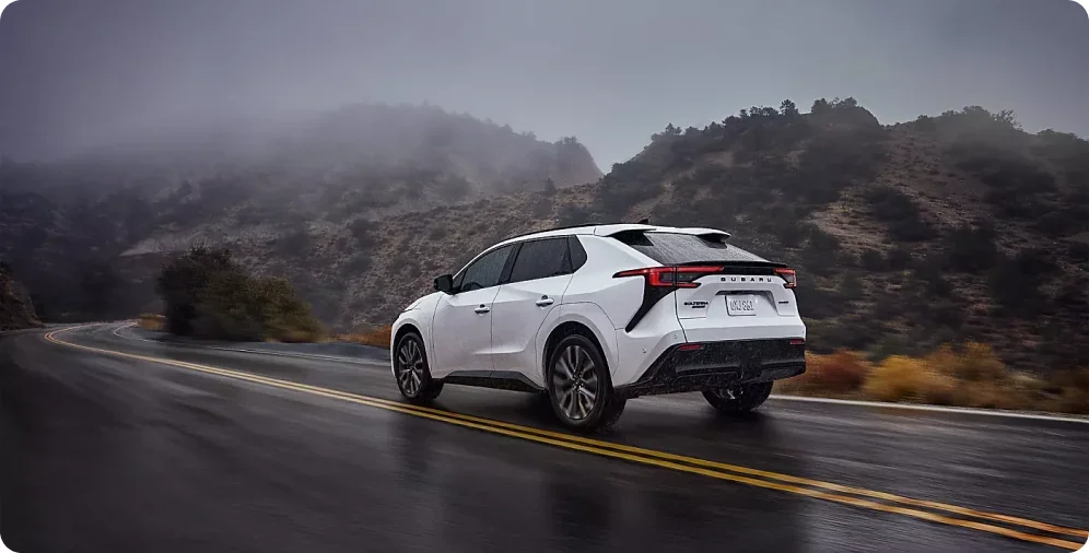 White 2026 Subaru Solterra XT accelerating along a wet canyon road