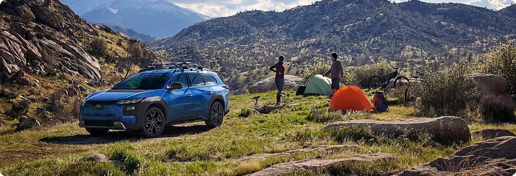 Campers pitching a tent beside a 2026 Subaru Trailseeker in the mountains