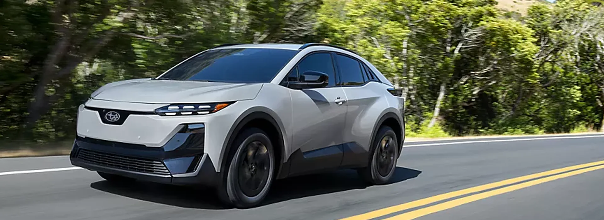 2026 Subaru Uncharted electric crossover driving a tree-lined road