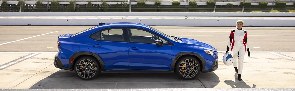 Blue 2026 Subaru WRX on a racetrack as a driver in a race suit walks past