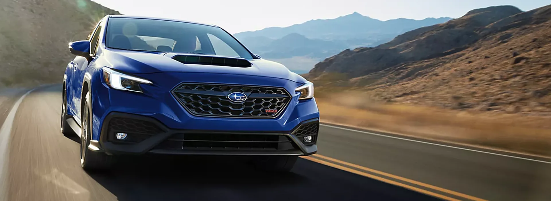 Blue 2026 Subaru WRX sports sedan cornering on a mountain highway