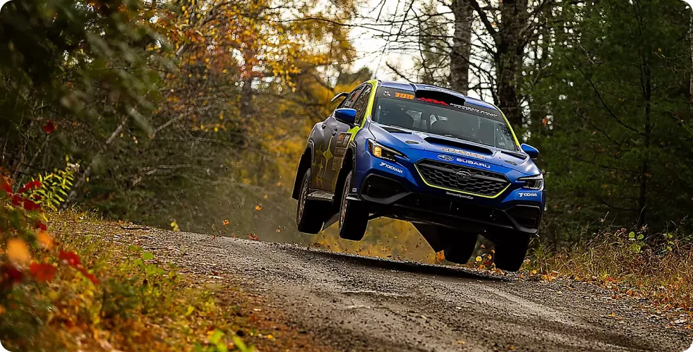Blue Subaru WRX rally car airborne on a forest gravel stage