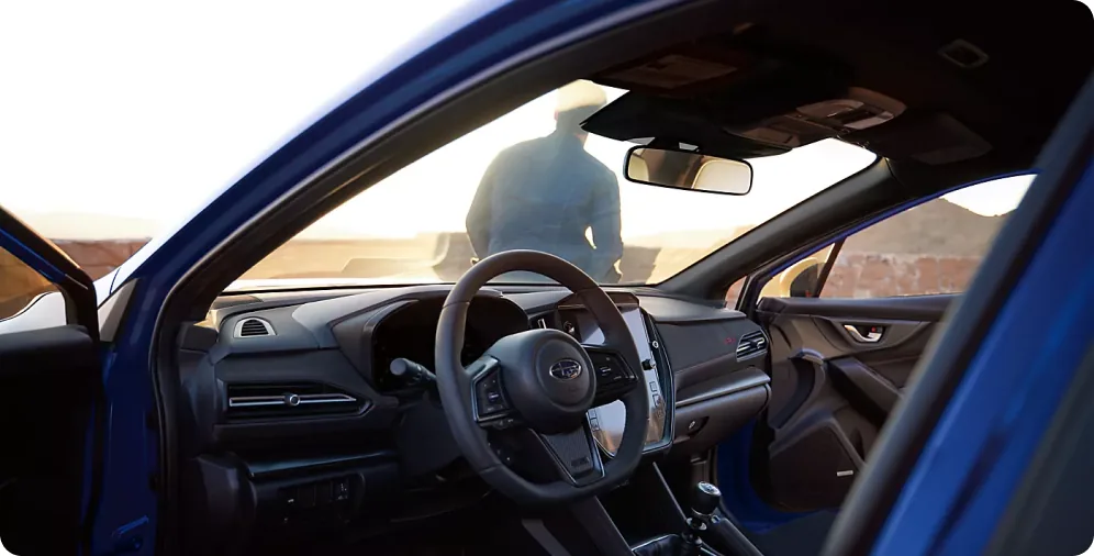 D-shaped steering wheel and cockpit of the 2026 Subaru WRX seen through the open driver door