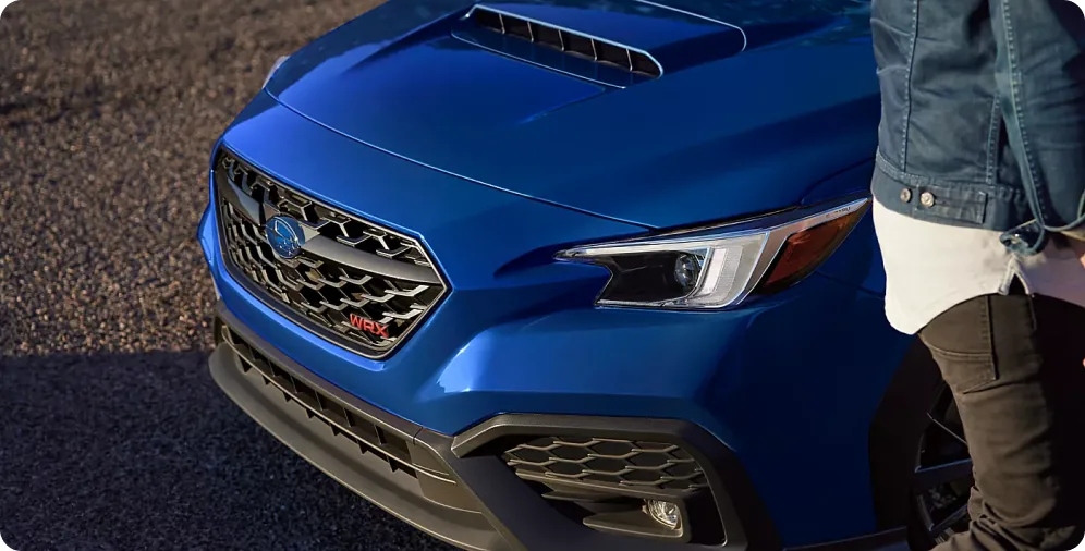 Front grille and headlight of a blue 2026 Subaru WRX with its owner standing alongside
