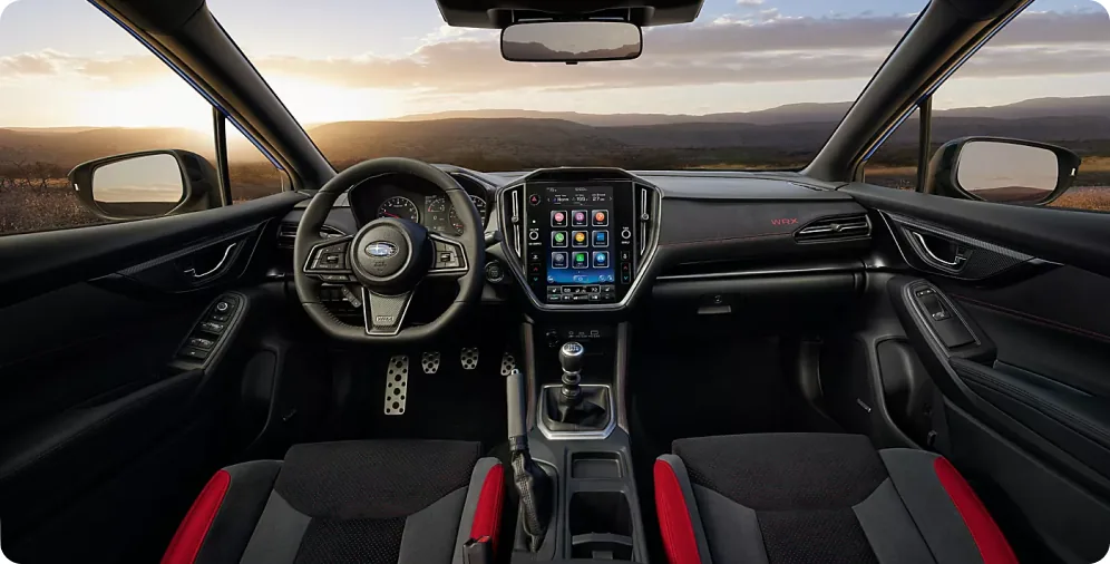 Driver-focused cabin of the 2026 Subaru WRX at sunset, with the D-shaped wheel and 11.6-inch touchscreen