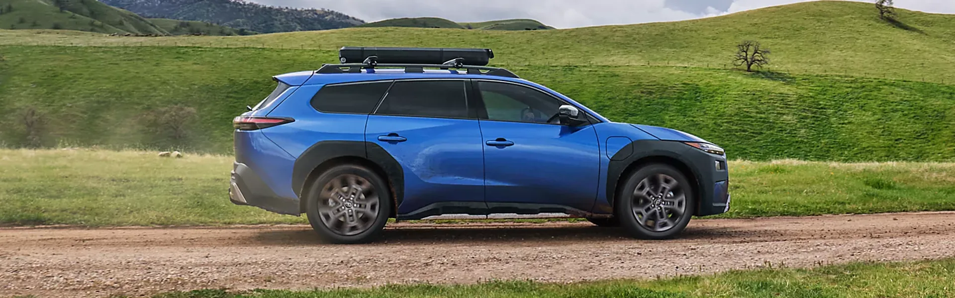 Blue Subaru Outback Wilderness on a gravel road through rolling green hills