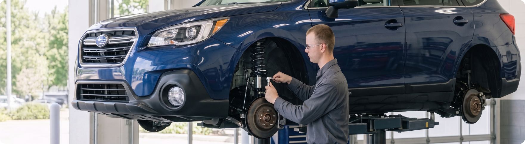 Briggs Subaru of Topeka technician inspecting the front suspension of a Subaru Outback on the lift