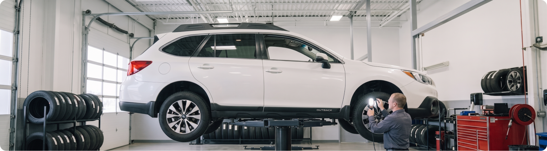 Briggs Subaru of Topeka technician checking suspension components under a raised Subaru Outback in Topeka, KS